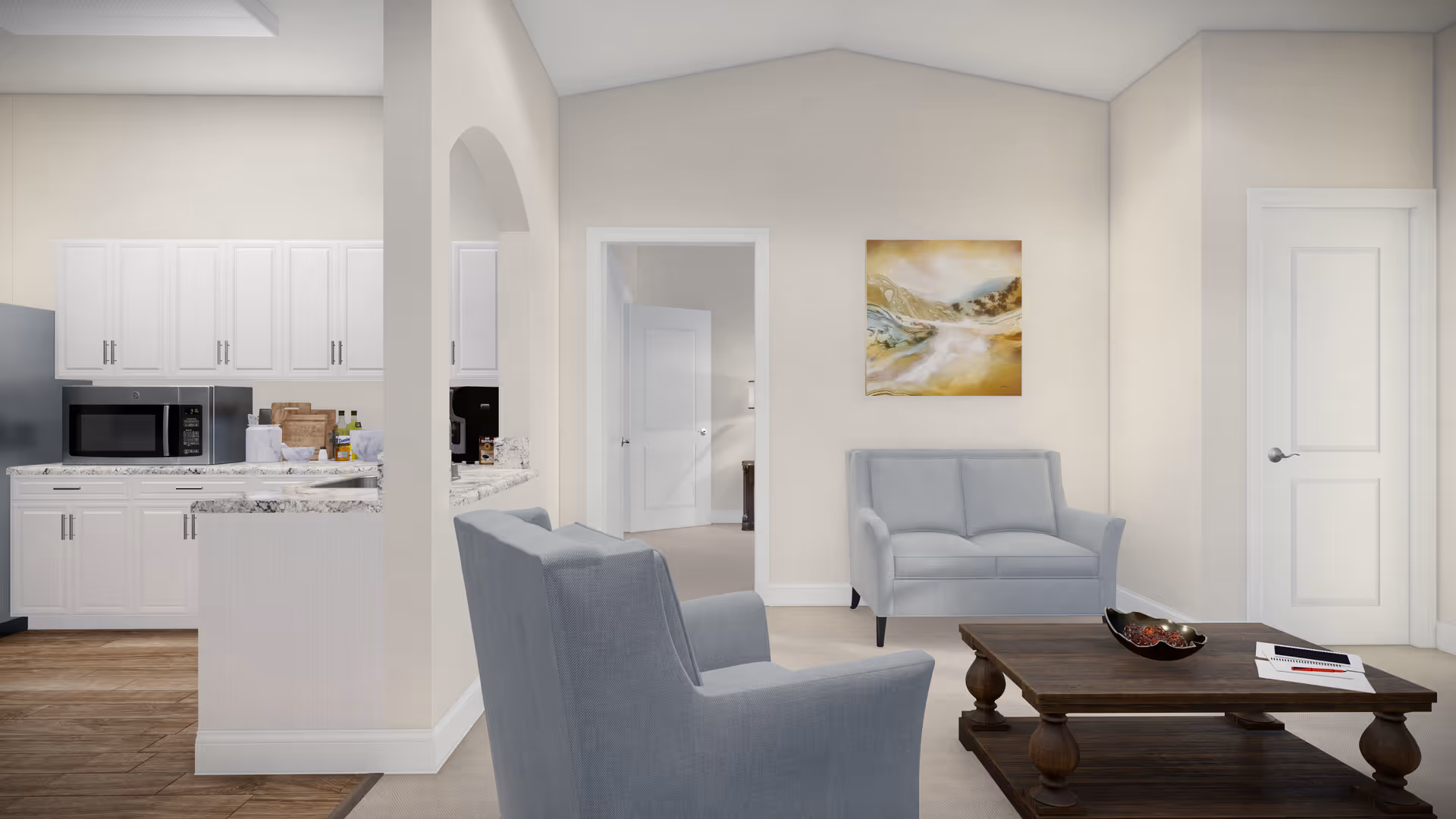 A bright and modern living room area with light gray armchairs and a matching loveseat. A dark wooden coffee table sits in the center with a decorative bowl and some papers on it. The walls are painted a soft beige, and a landscape painting hangs above the loveseat. To the left, there is a partial view of a kitchen with white cabinets, a microwave, and a marble countertop. The floor is wooden, and there are two white doors visible in the background.