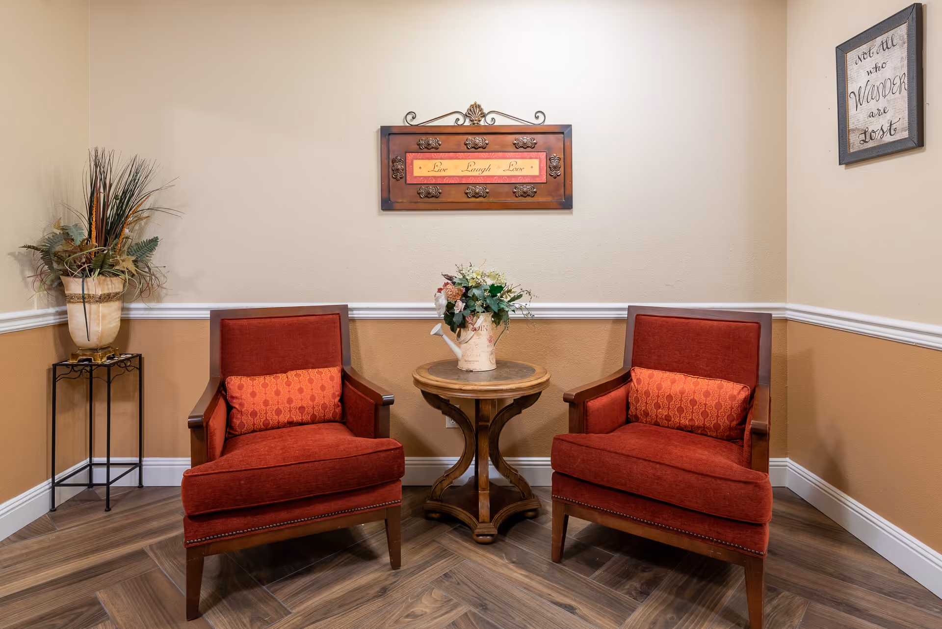 Two red upholstered armchairs flank a round wooden side table with a floral arrangement in a cozy seating nook.
