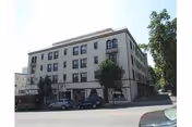 Exterior view of a multi-story beige building with several windows and small balconies, identified as Bret Harte Retirement Inn, with trees and parked cars along the street in front.