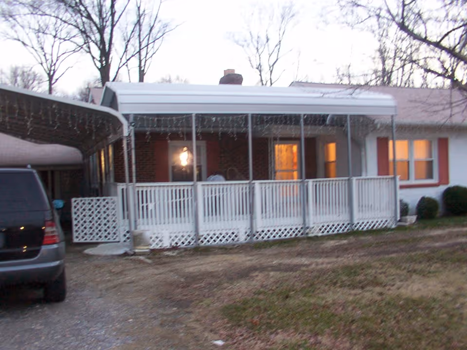 Front exterior of a single-story house with a covered porch and white railing and a car parked in the driveway.