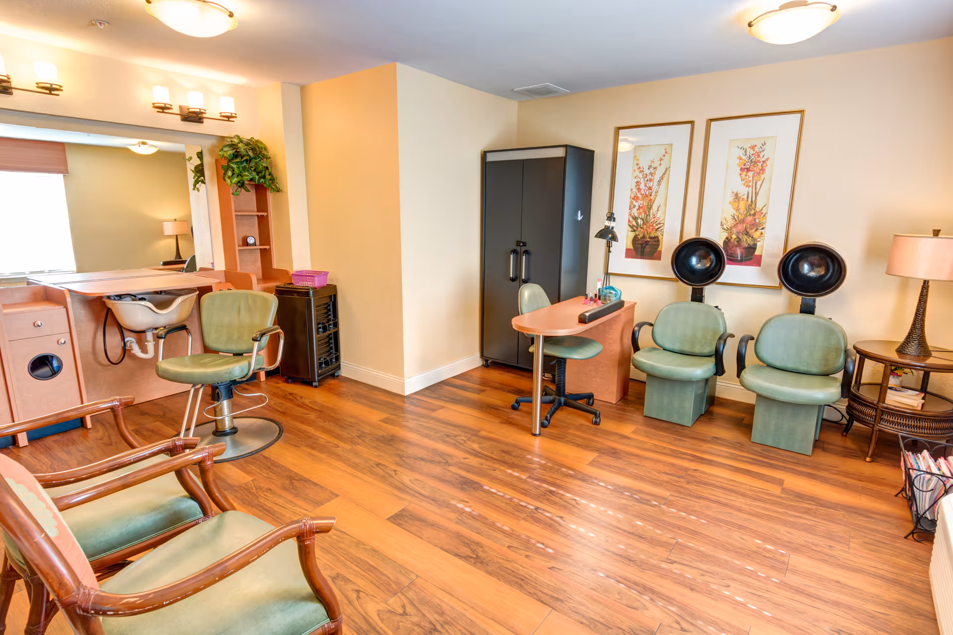 Bright salon-style common room with hair styling chairs, hooded dryers, a shampoo sink, and a manicure station.