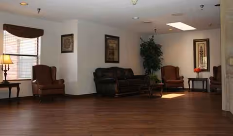 A spacious senior living lounge with brown leather couches and a potted plant.