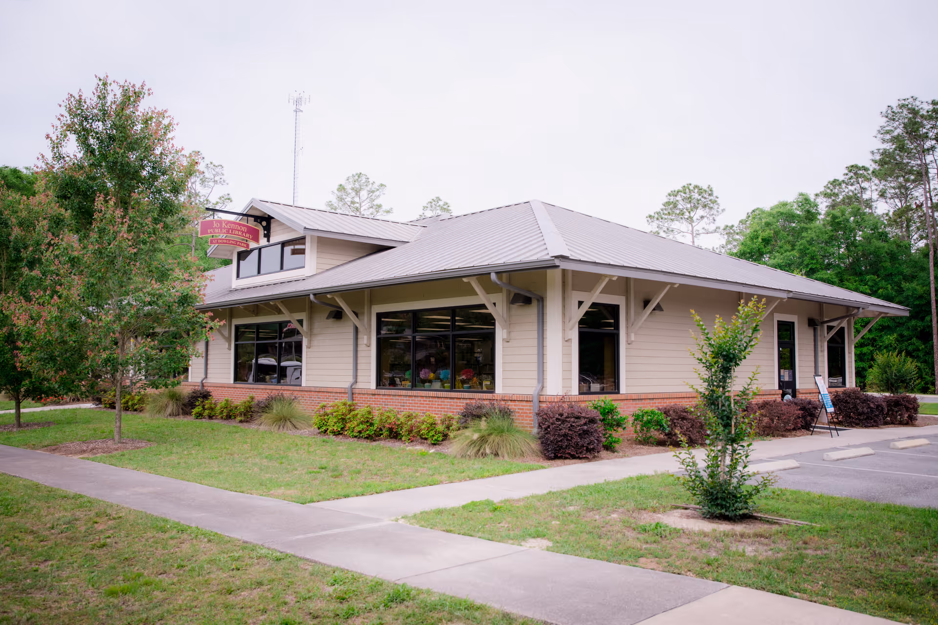 One-story community building with a metal roof, large windows, and surrounding landscaping viewed from the front.