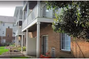 Exterior view of a brick senior living building with balconies and trees.