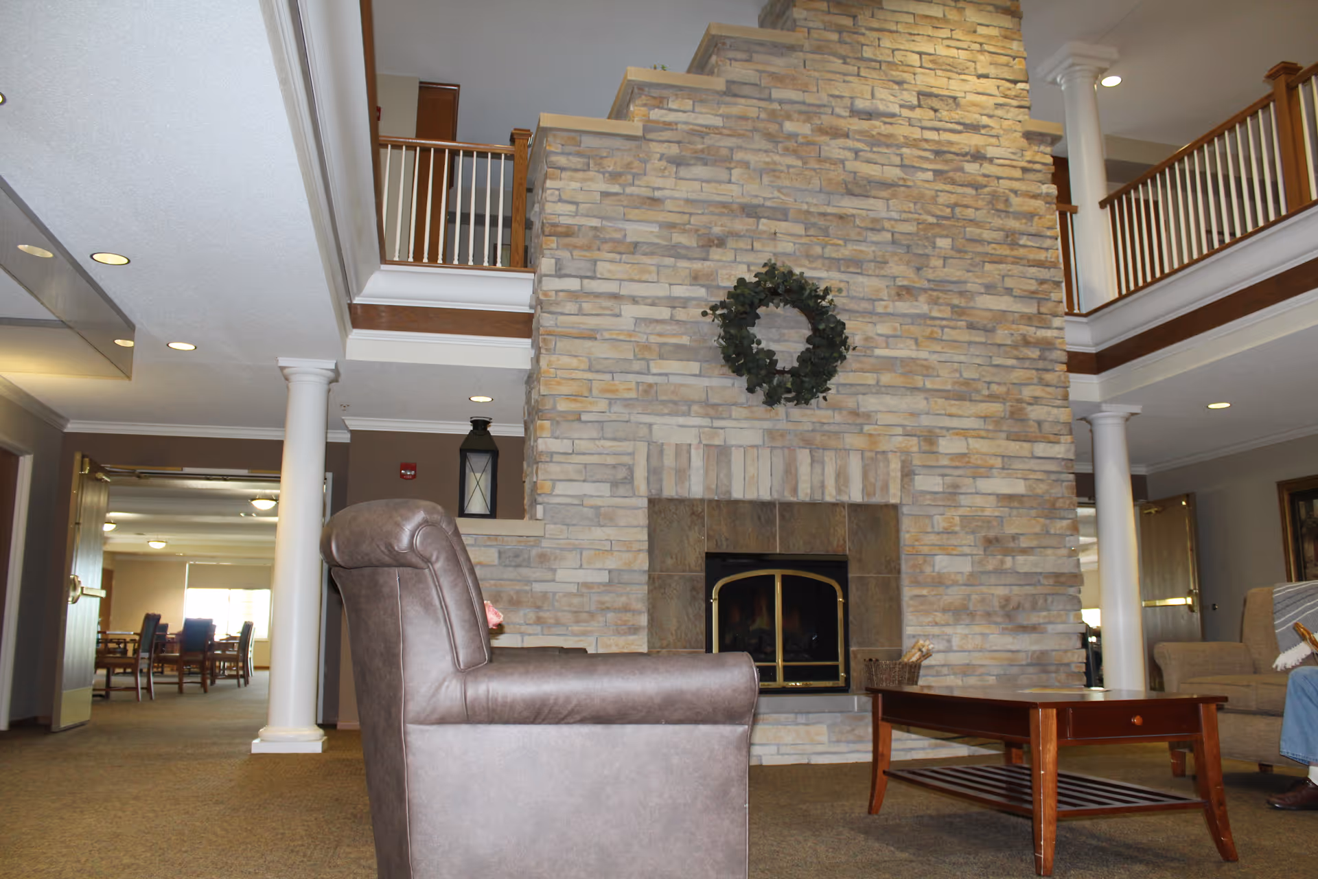 Two-story common lounge with a large stone fireplace, seating, a coffee table, and upper balcony railings.