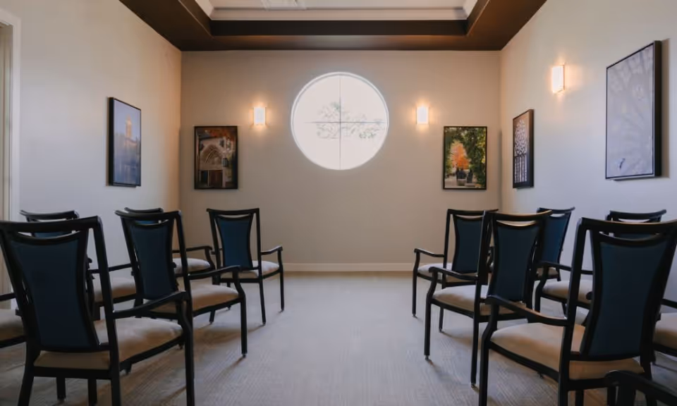 Small meeting room with rows of chairs facing a round window and framed artwork on the walls.