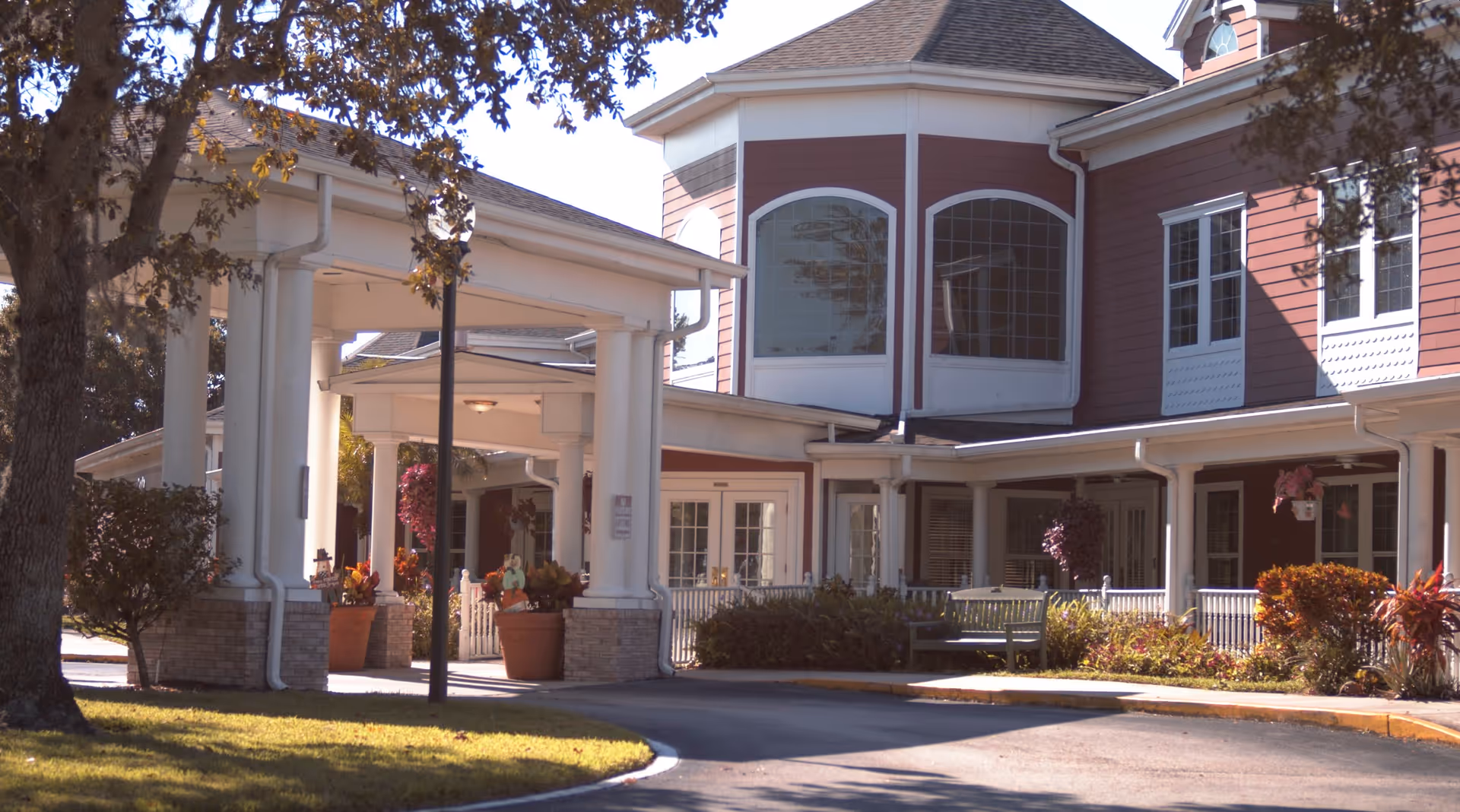 Exterior view of Spring Hills Hunters Creek facility showing a covered entrance with white columns, large windows, and landscaped bushes and trees around the building.