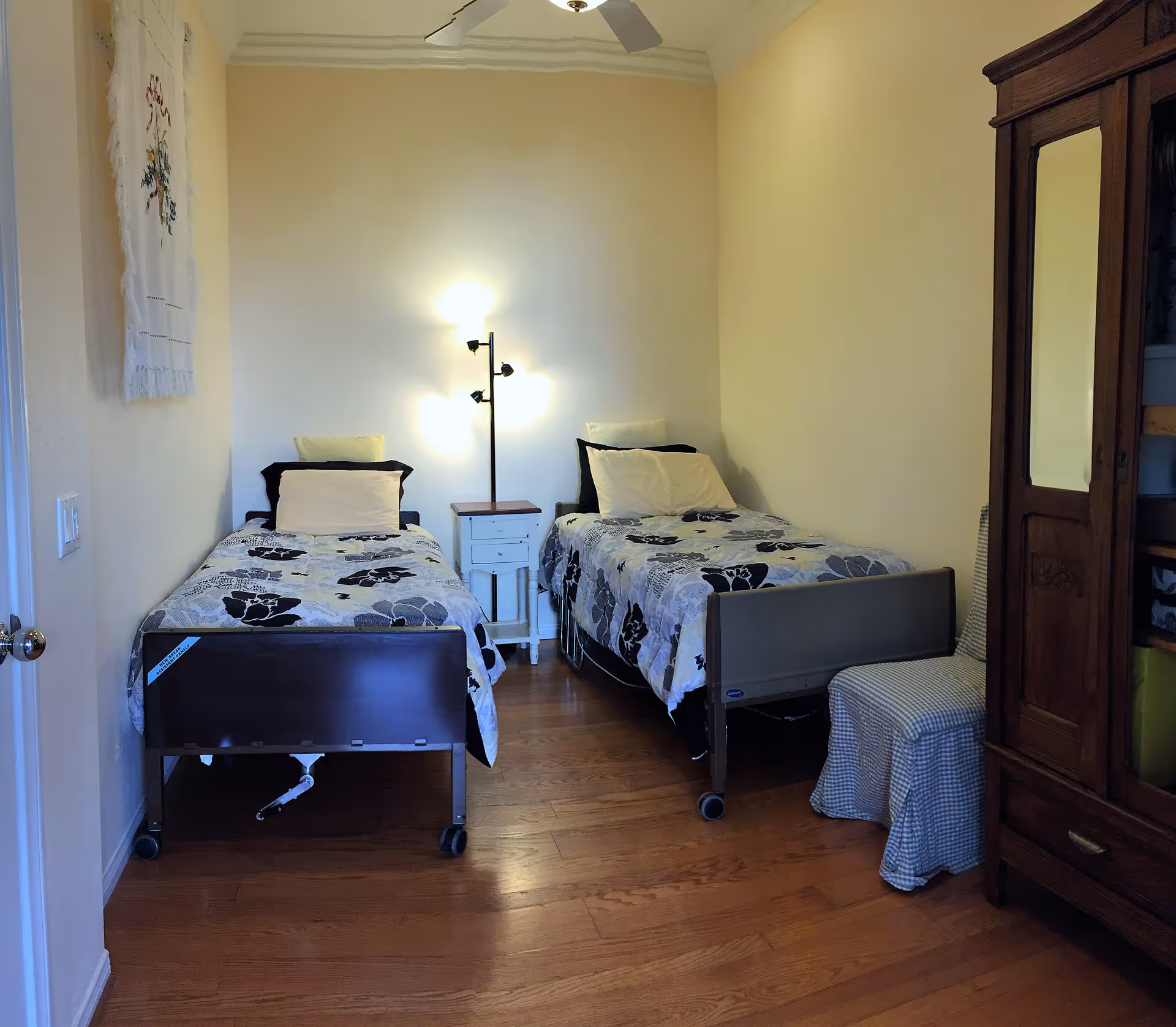 Two twin beds with matching bedding and a nightstand fill a small, well-lit bedroom.