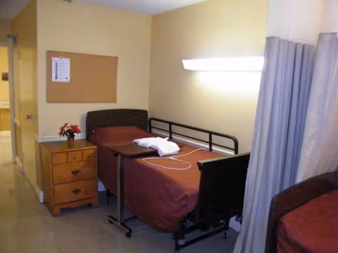 A hospital-style bedroom in a nursing center with beds, a nightstand, and a privacy curtain.