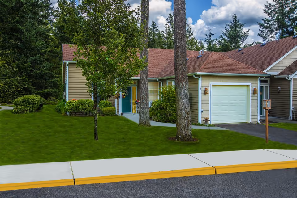 Exterior view of a single-story residential unit with beige siding, a green front door, a garage with a white door, and a well-maintained lawn with trees and shrubs. The sky is partly cloudy.