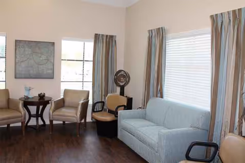 Bright senior living lounge with blue sofa, chairs, curtains, and windows