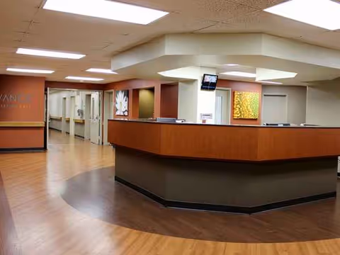 Lobby reception area with a curved wooden desk and hallway in a senior facility.