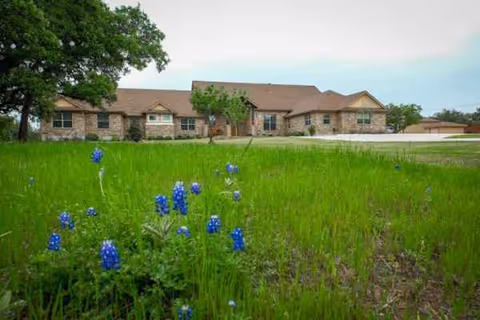 Front exterior of a senior living facility with a green lawn and blue flowers.