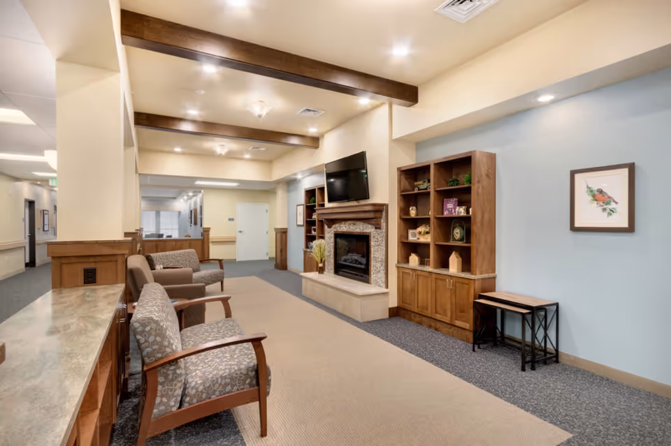 Cozy common room with armchairs, a fireplace and wall-mounted TV flanked by wooden shelving.