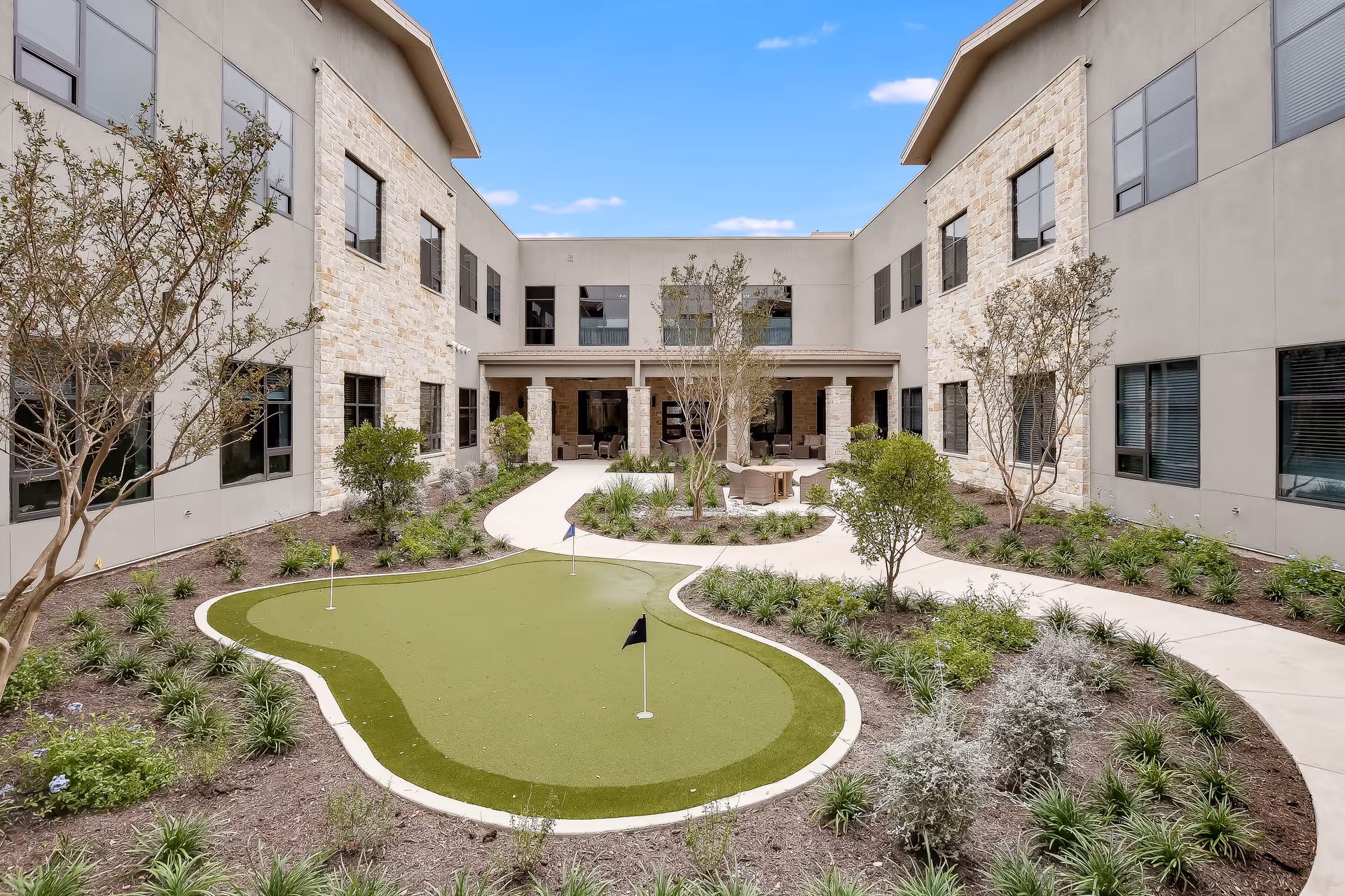 A landscaped interior courtyard with a small putting green, winding walkways, seating area, and a two-story building surrounding it.