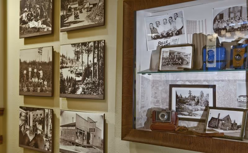 A wall display featuring several framed black-and-white vintage photographs and a glass case containing old cameras and more framed photos, showcasing historical scenes and people.