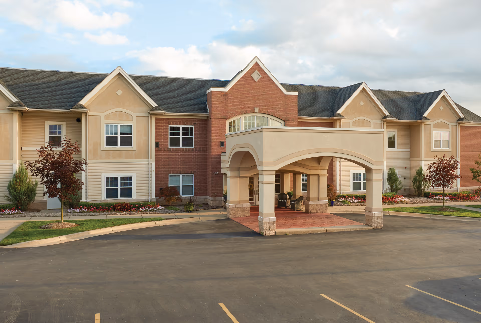 Front entrance of a two-story senior living building with a covered porte-cochère and landscaped grounds.