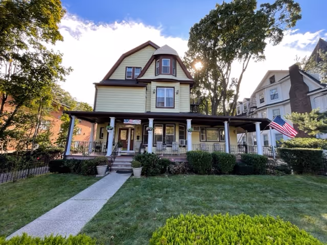Front view of The Willows Home exterior, yellow two-story house with wide porch and lawn.