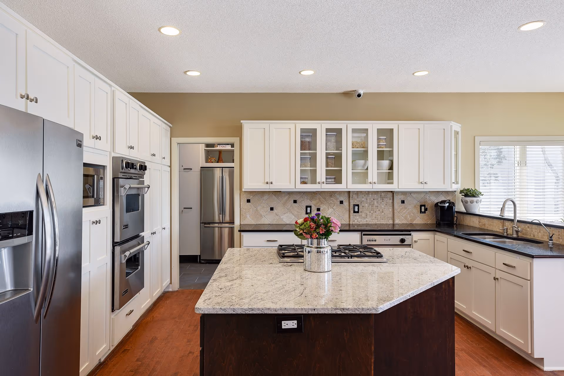 Spacious modern kitchen with a large marble-topped island, white cabinets, stainless steel appliances, and a vase of flowers.