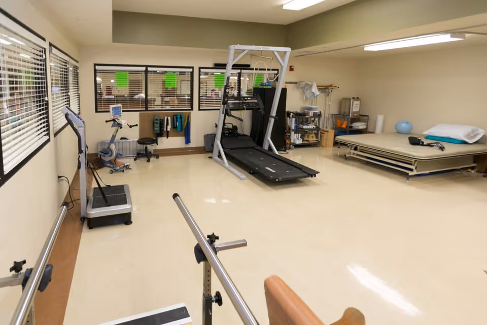 Spacious physical therapy room with parallel bars, a treadmill, exercise machines, and therapy beds and equipment.