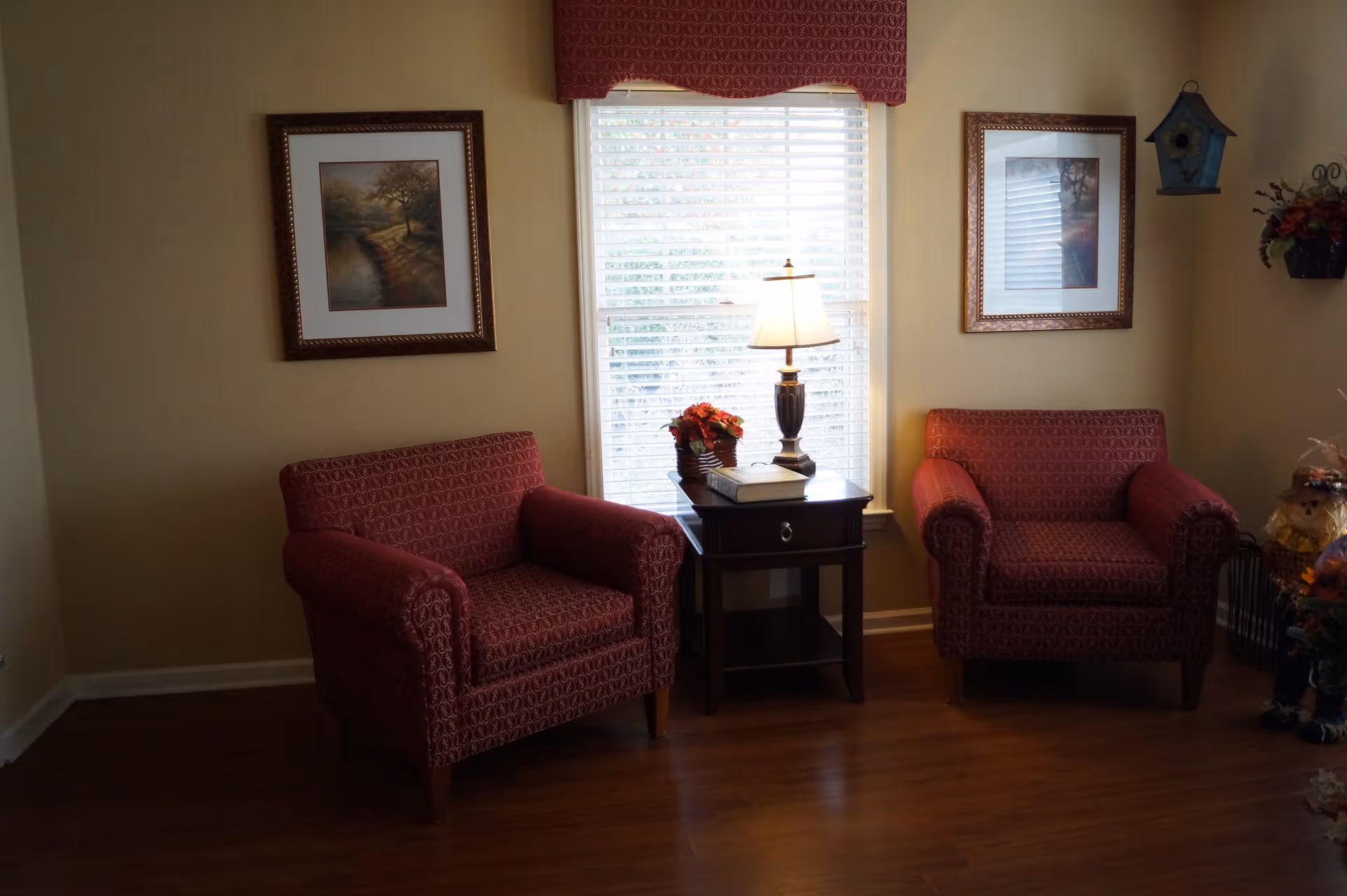 Two patterned armchairs flanking a side table with a lamp in front of a window in a cozy sitting area.