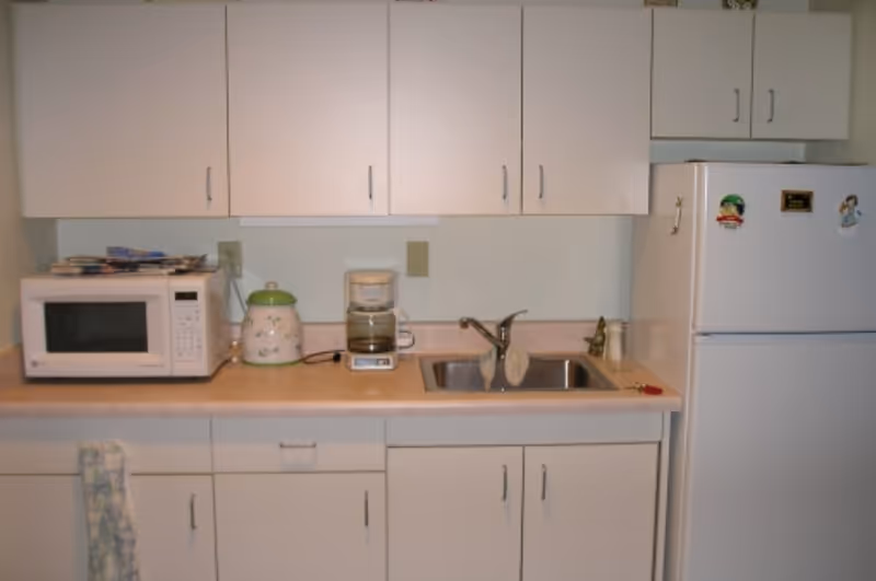 Small kitchenette with white cabinets, a microwave, coffee maker, sink, and refrigerator.