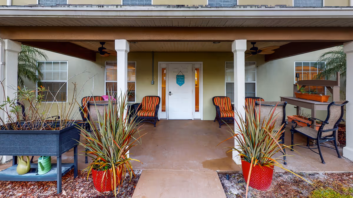 Covered front entrance patio with potted plants, wicker chairs, and a white entry door.