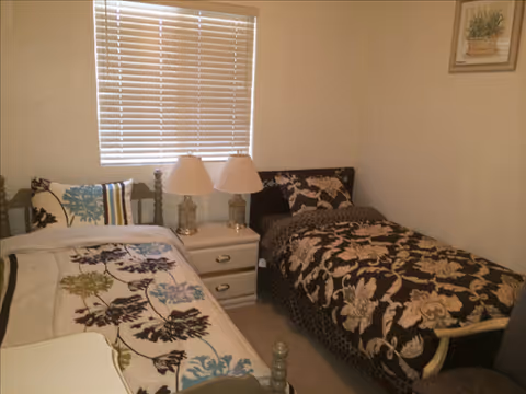 Two twin beds with patterned quilts and a shared nightstand in a small bedroom.