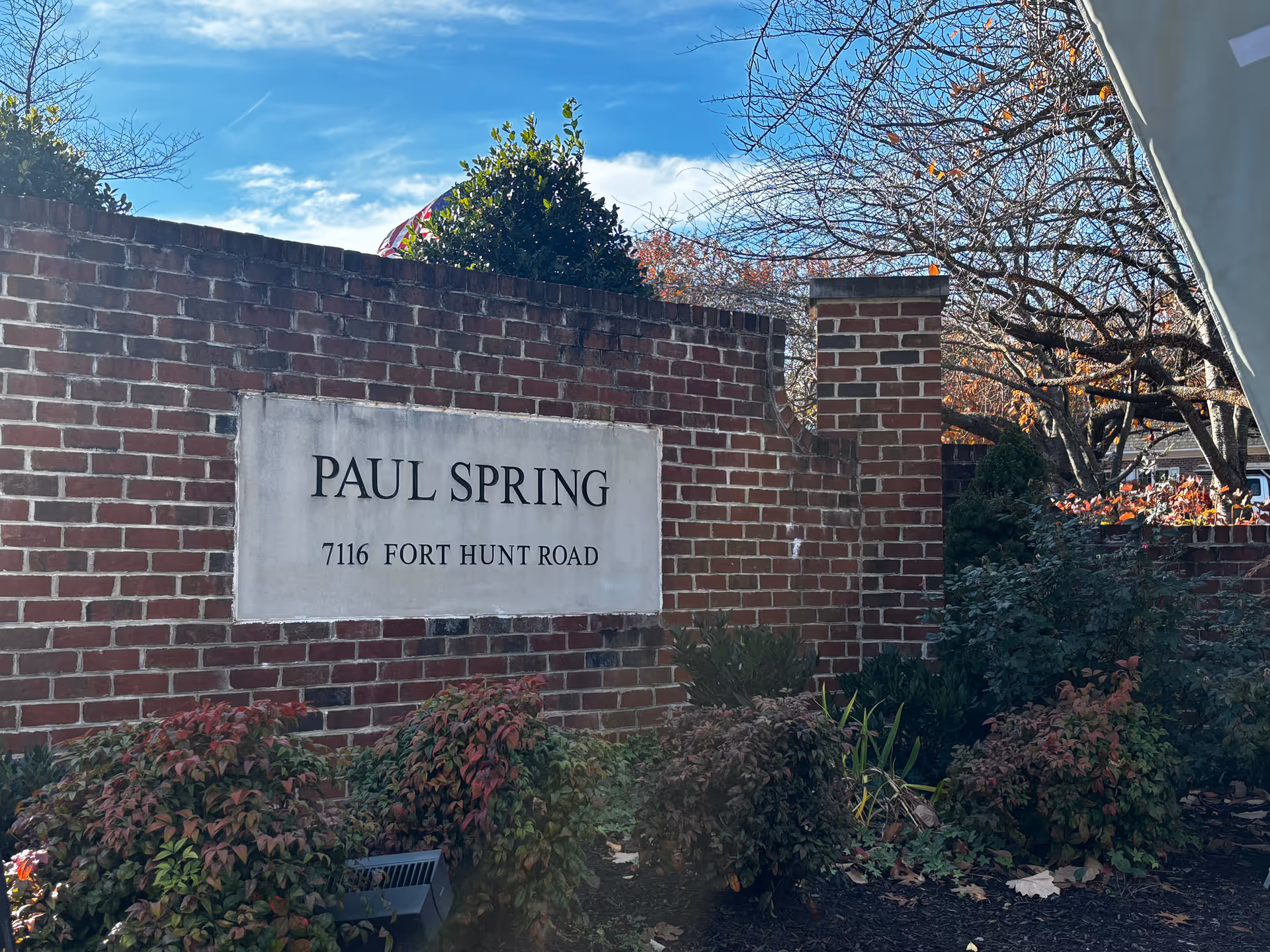 Brick entrance sign that reads 'PAUL SPRING 7116 FORT HUNT ROAD' with landscaping and trees in the background.