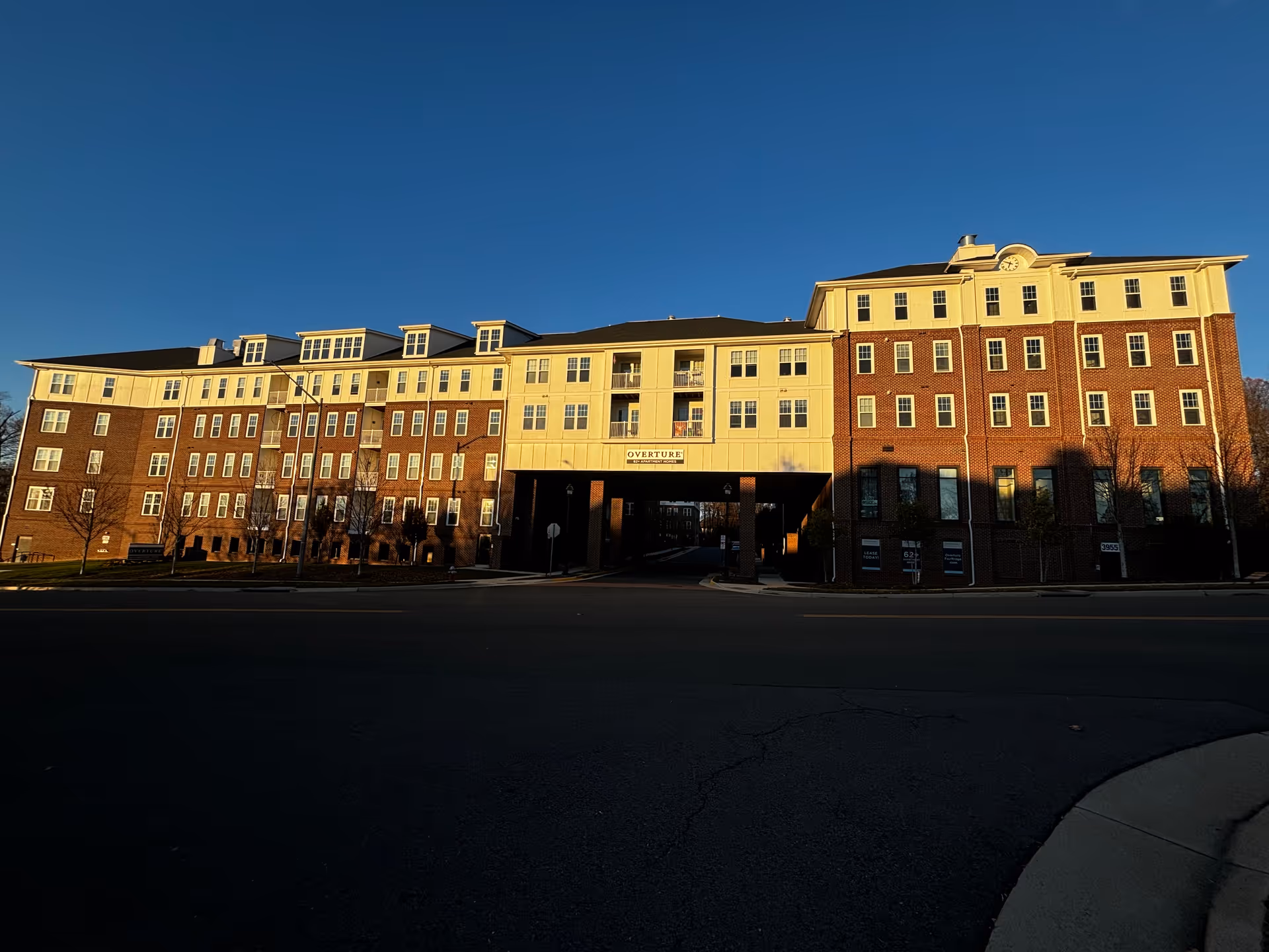 Exterior view of a large multi-story senior living facility building named Overture Fair Ridge, with a clear blue sky above and sunlight casting shadows on the brick and cream-colored facade.