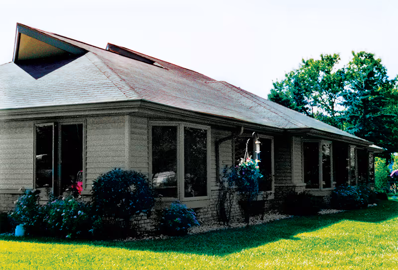 Single-story assisted living building exterior showing large windows, shrubs, and a grassy lawn.