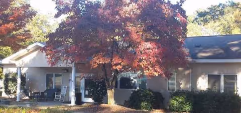 Single-story senior living facility front with autumn trees and a small porch entrance.
