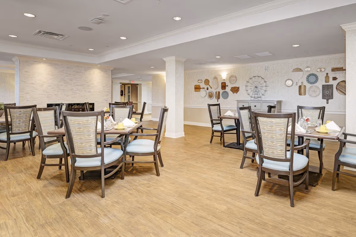 Bright dining room with multiple wooden tables and chairs on wood-look flooring and decorative wall art.