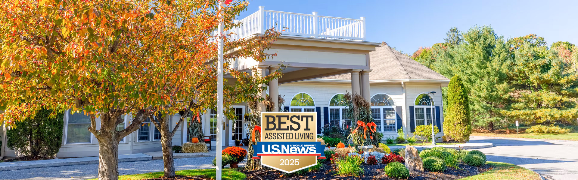 Front exterior view of Benchmark at Haverhill Crossings facility with autumn trees, landscaping, and a sign displaying 'Best Assisted Living U.S. News 2025'.