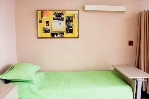 A single bed with green cover sits in a pastel senior living bedroom.