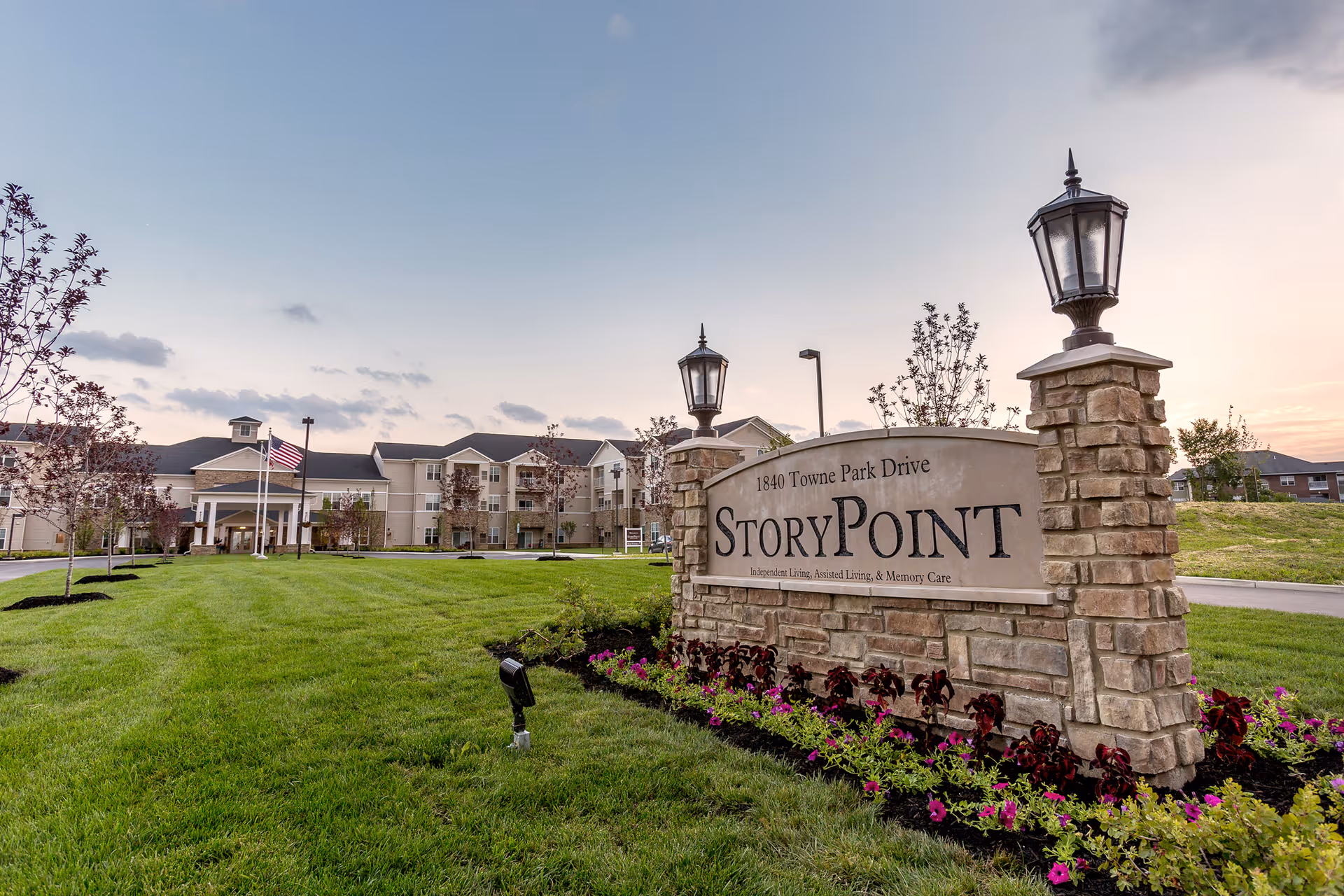 Stone entrance sign reading 'StoryPoint' in front of a landscaped lawn and a multi-story senior living building at sunset.