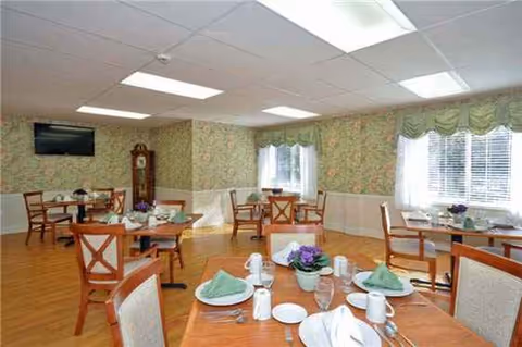 A dining room with round tables set for meals in a sunny, floral-walled facility.