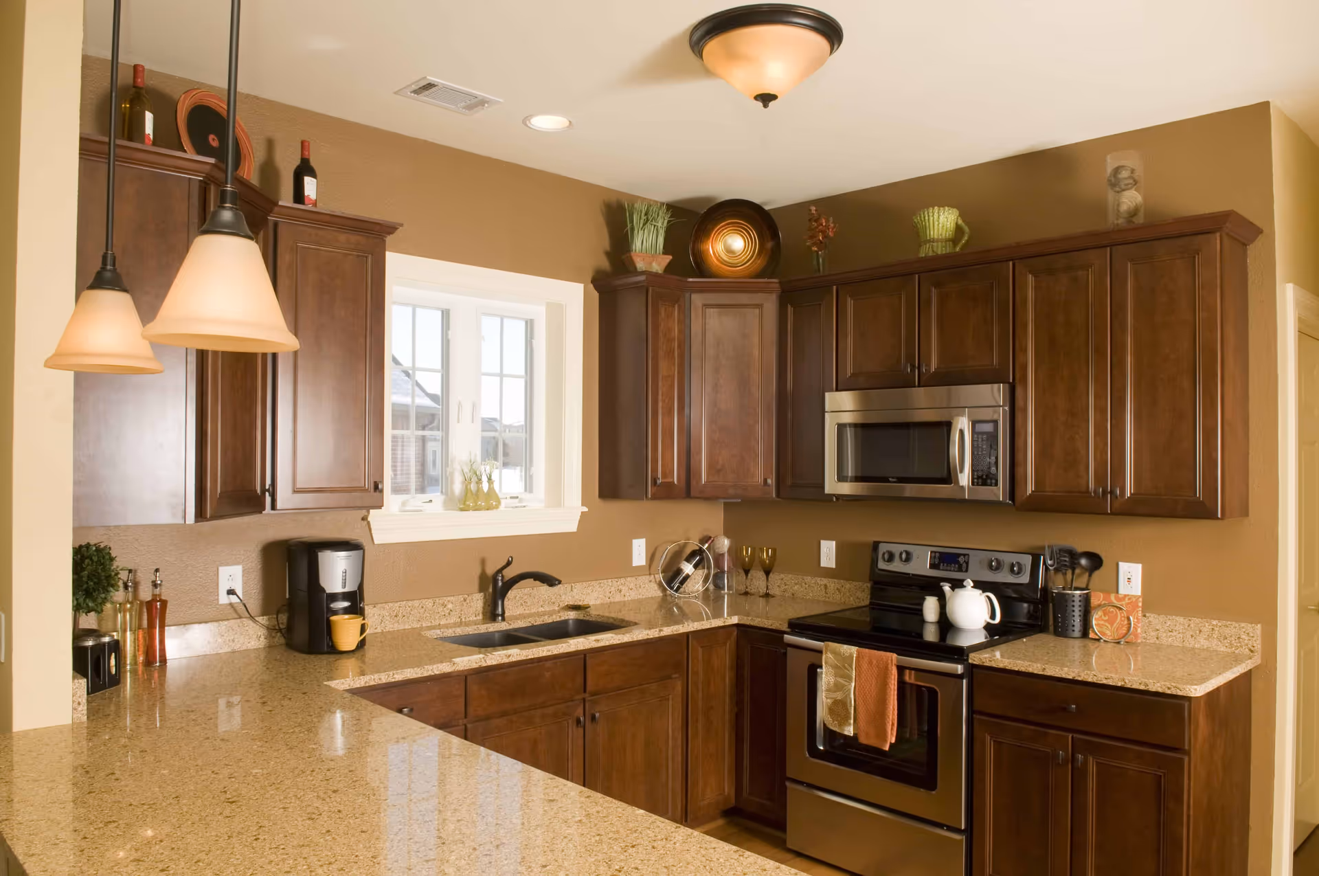 Modern kitchen with dark wood cabinets, granite countertops, a stainless steel stove and microwave, a sink under a window, and pendant lighting.
