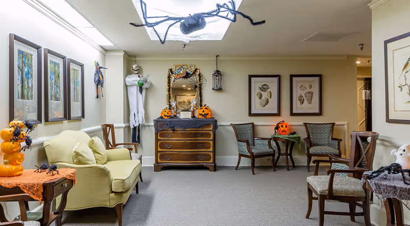 A communal sitting room with sofas and chairs decorated for Halloween with pumpkins, cobwebs, and a hanging ghost.