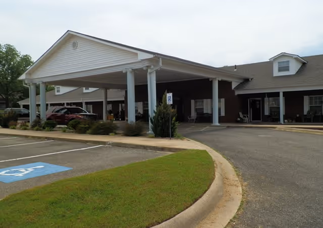 Exterior view of Clarksville Retirement Center showing a covered entrance with white columns, a driveway, parking spaces including a handicapped spot, and part of the building with windows and doors.