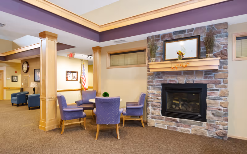 Cozy communal lounge with purple upholstered chairs arranged around a table next to a stone fireplace.