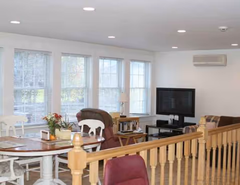 Bright senior living living room with seating, a round dining table, TV, and large windows.