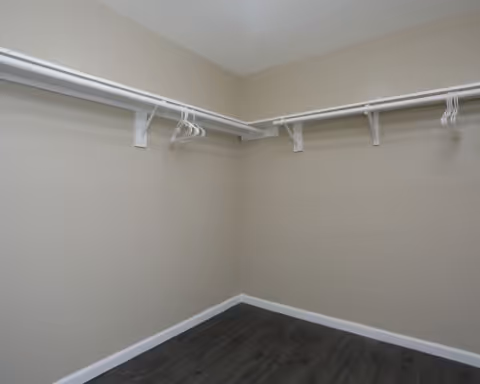 Empty walk-in closet with beige walls, white hanging rods and a dark wood floor.