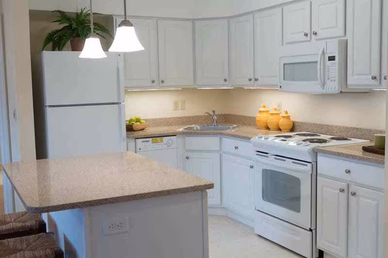 Bright kitchen with white cabinets, refrigerator, stove, microwave, sink and a central island countertop.