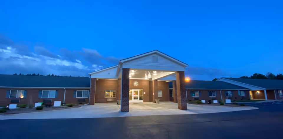 Exterior front view of Wexford House senior living facility at dusk, showing a brick building with a covered entrance and lit windows under a blue sky.