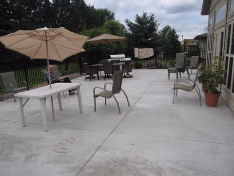 Outdoor patio with tables, chairs, umbrellas, a grill, and potted plants beside a building.