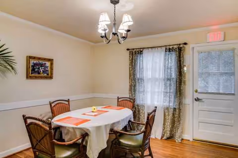 Val's Family Care Home dining room with a round table, four chairs, chandelier, and curtains.