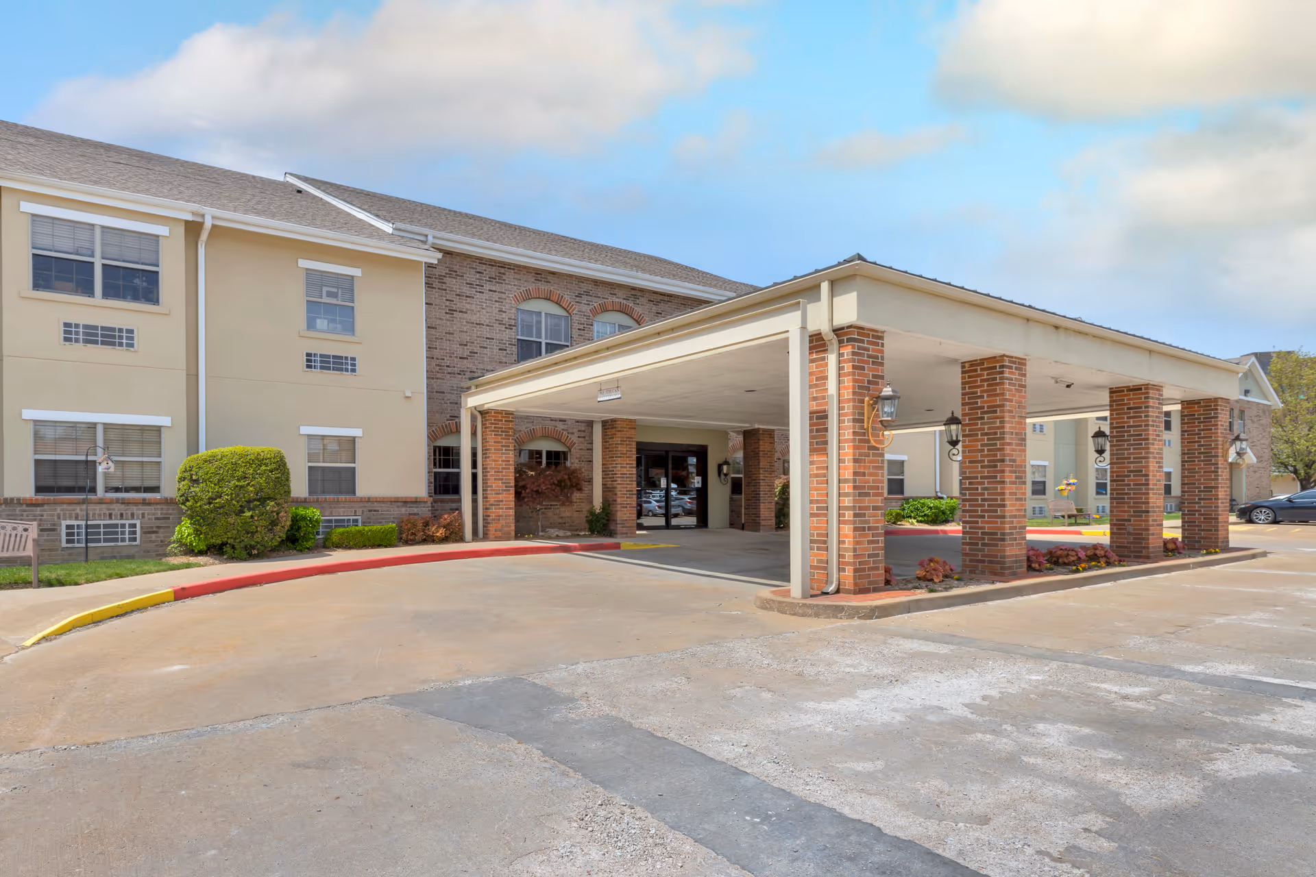 Covered brick portico entrance to a two-story assisted living building with a driveway and parking in front.