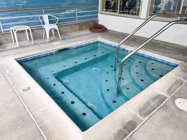 Square bubbling spa/hot tub with metal handrail and built-in steps next to chairs and a painted mural wall.