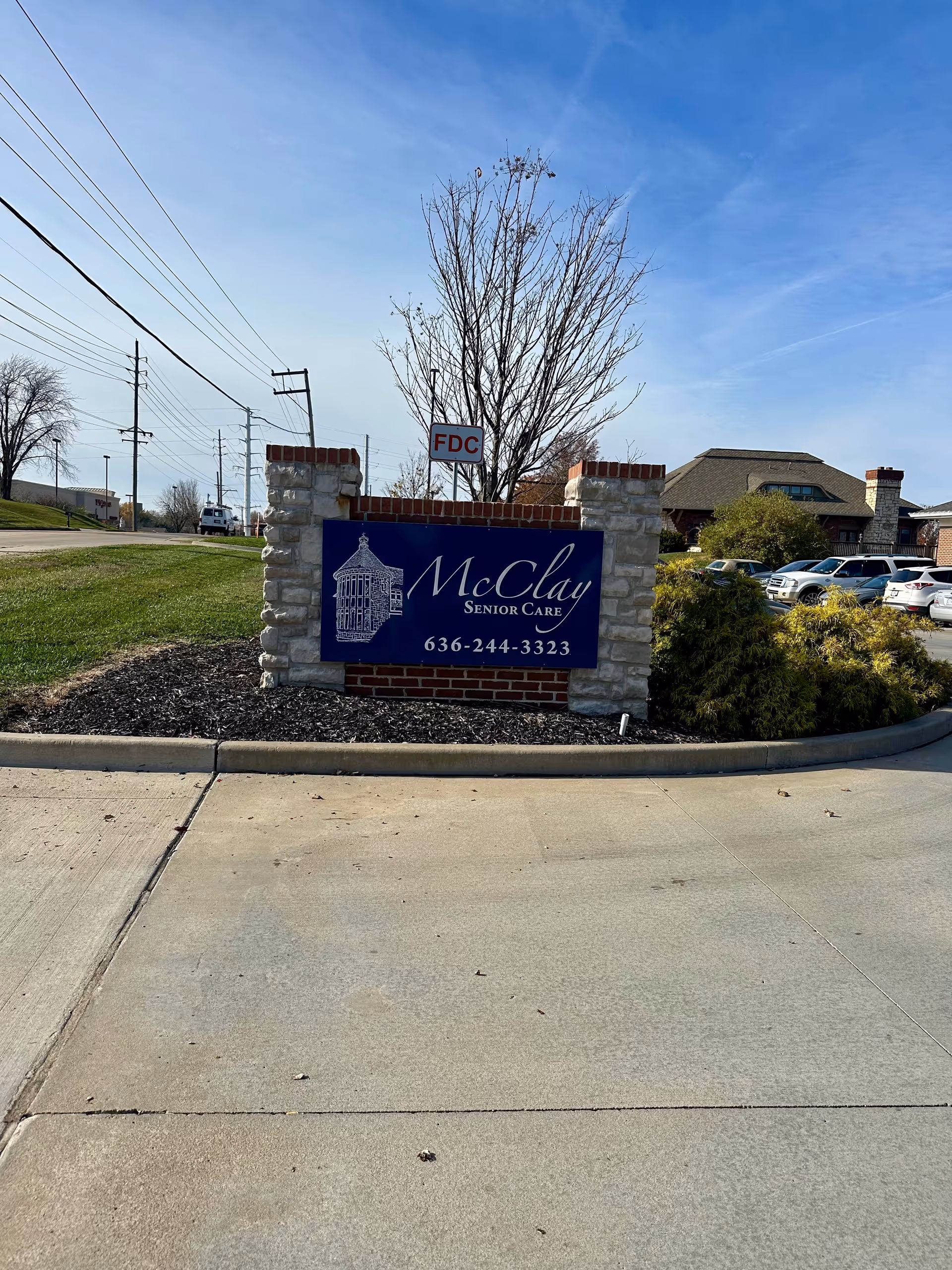 Stone and brick entrance sign reading 'McClay Senior Care' at a facility driveway with the building and parked cars in the background.